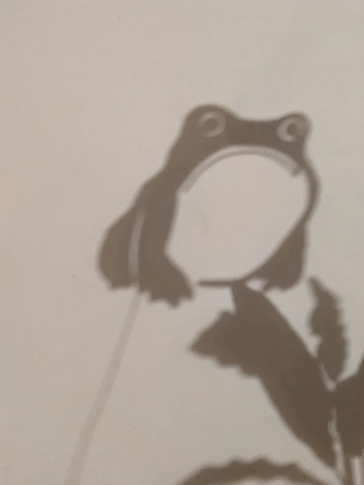 Brown frog shadow puppet head and body silhouette against beige background