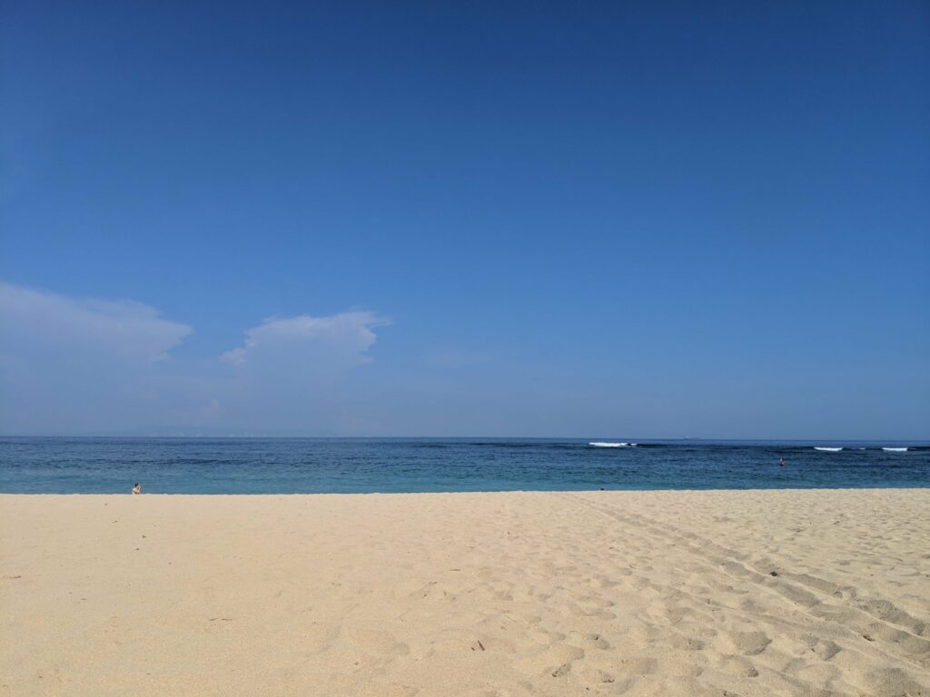 Beach landscape with sandy shore, calm ocean, and blue sky