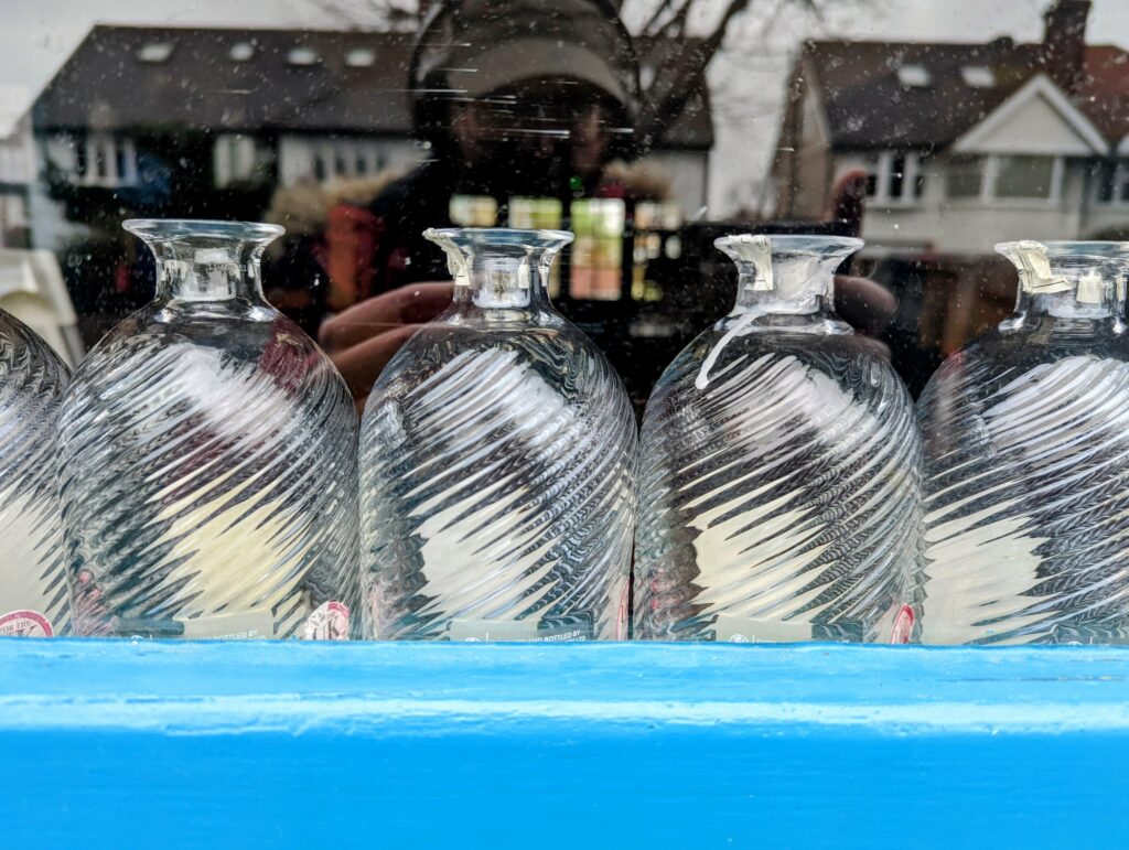 Four frosted glass bottles in snowy suburban setting with house in background