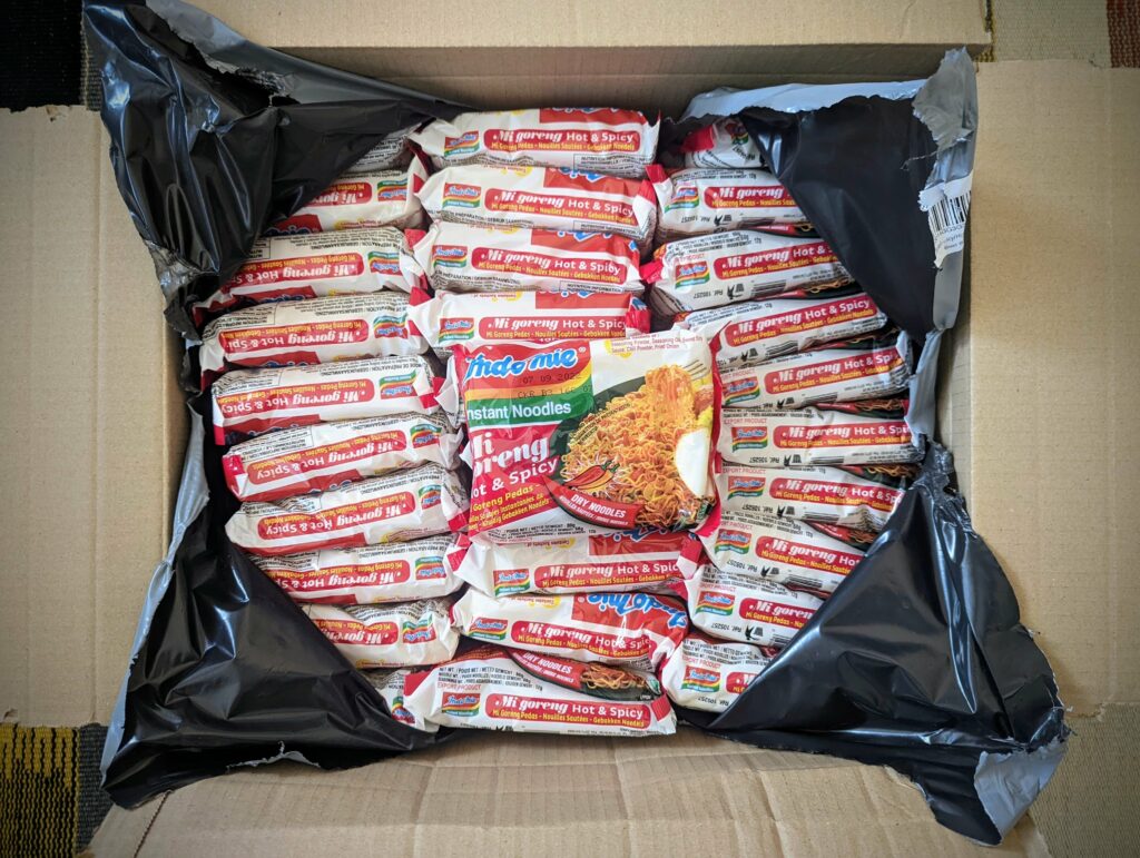 Box filled with packets of instant noodles with one open package displayed