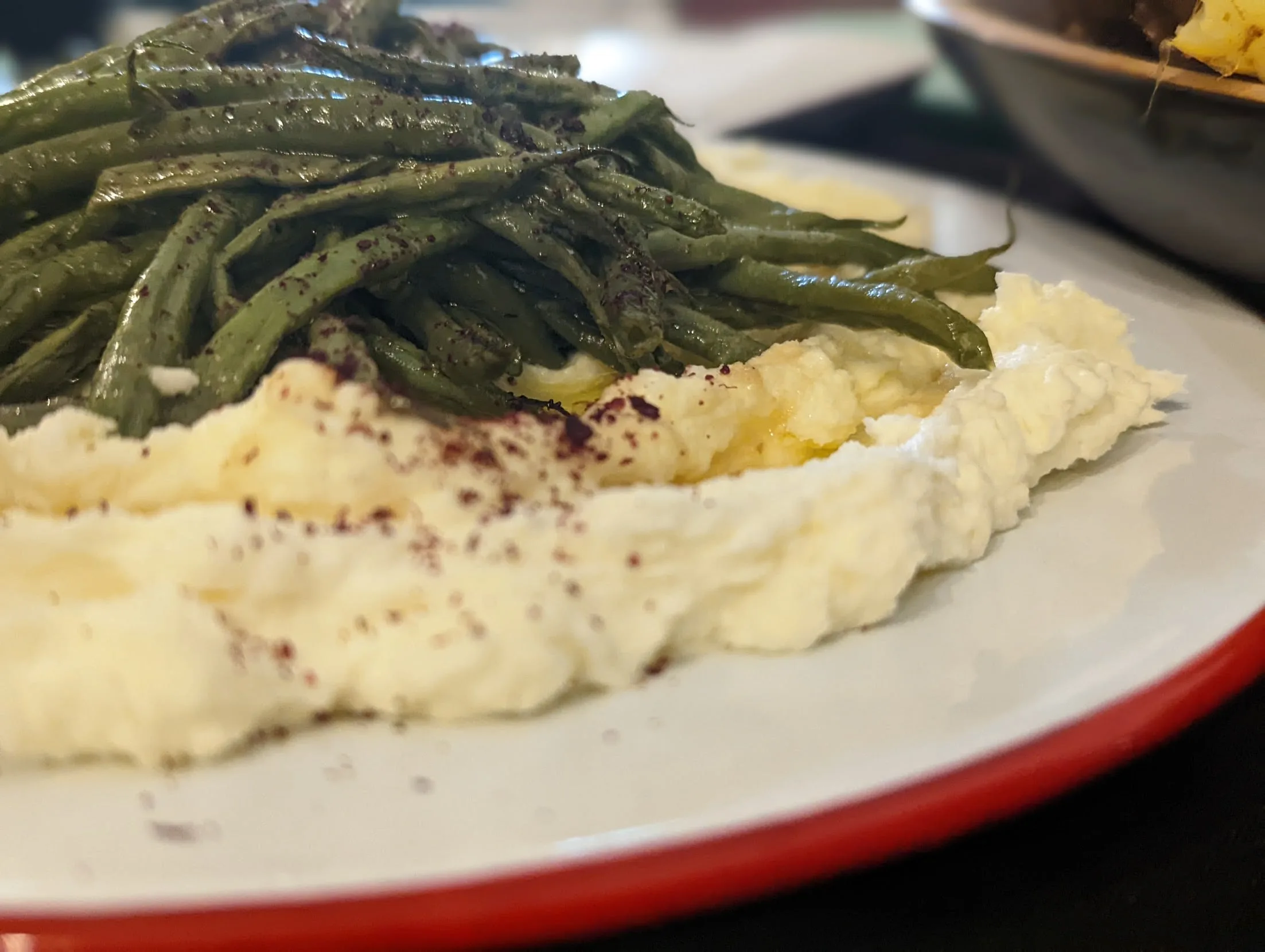 Mashed potatoes and green beans on white plate with red rim