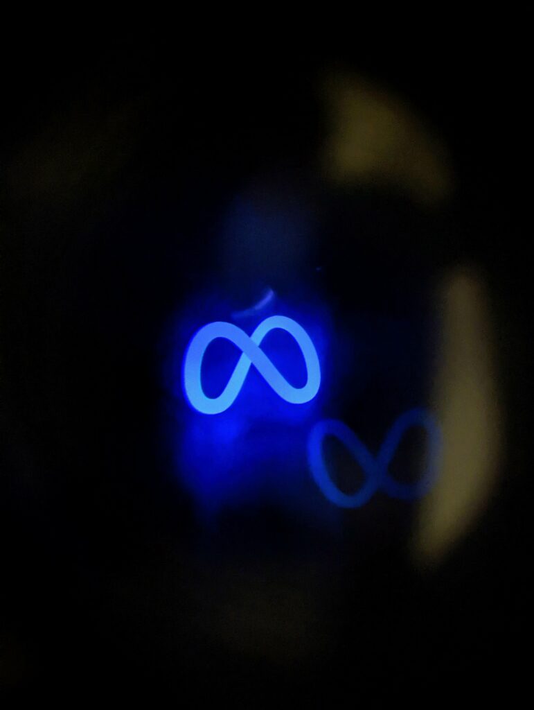 A glowing neon blue Meta infinity logo in a dark setting, with a secondary out-of-focus reflection to the right.