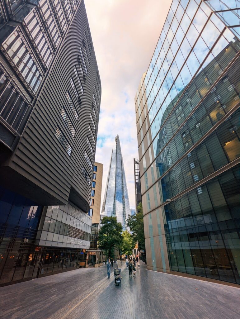 The Shard skyscraper framed by towering modern glass buildings along a pedestrian walkway in London.