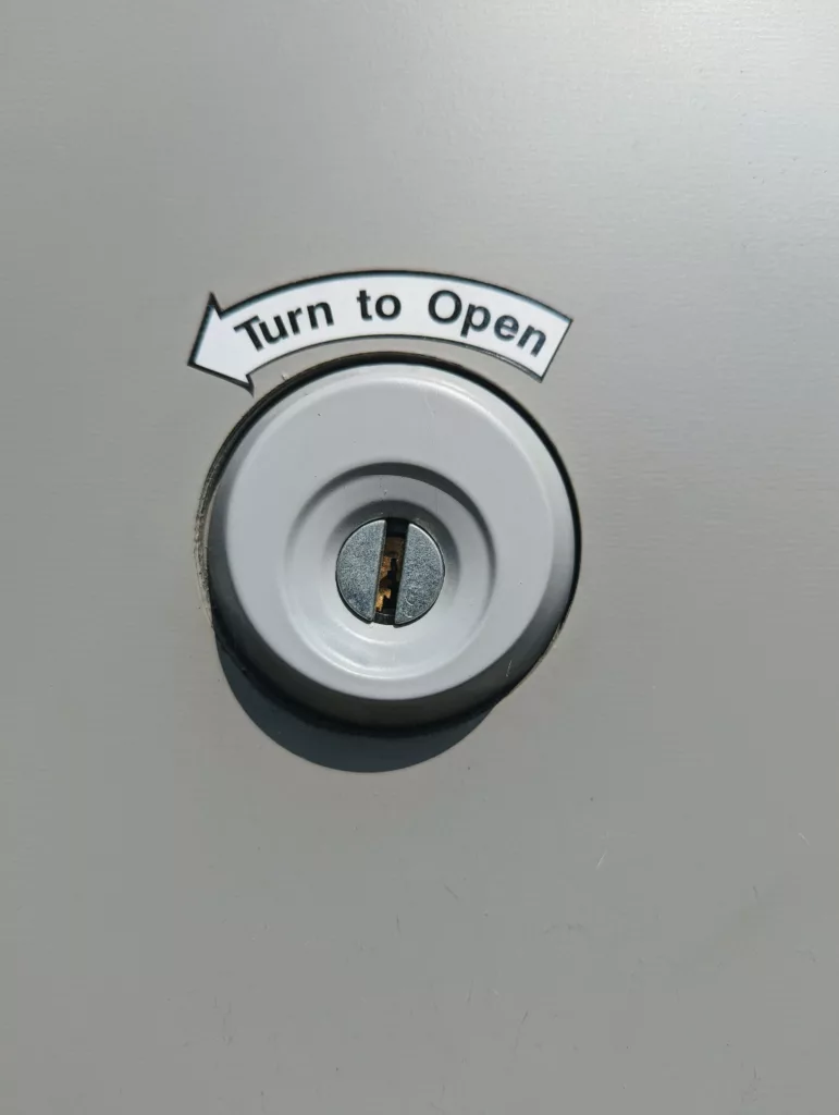 Close-up of a circular keyhole on a grey surface with a curved arrow above it pointing left and the text Turn to Open.