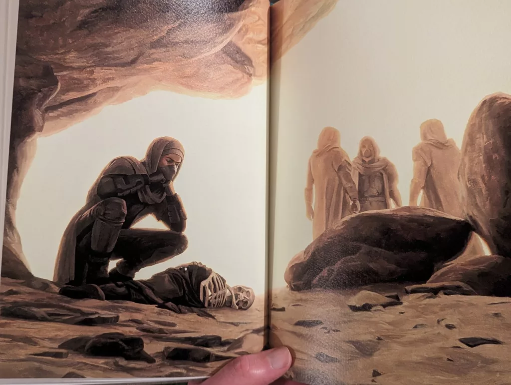 A robed figure in a mask crouches over a skeleton inside a cave, while three others stand in the bright desert landscape outside.