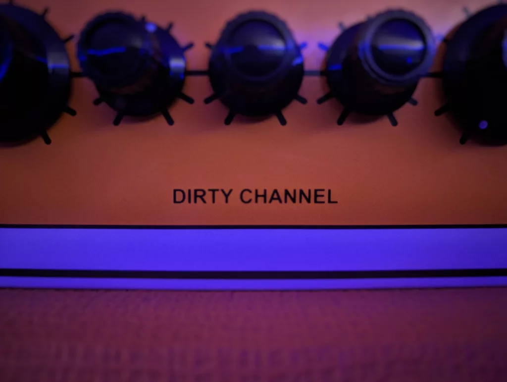 Black control knobs on an orange guitar amplifier panel labeled DIRTY CHANNEL, bathed in atmospheric blue light.