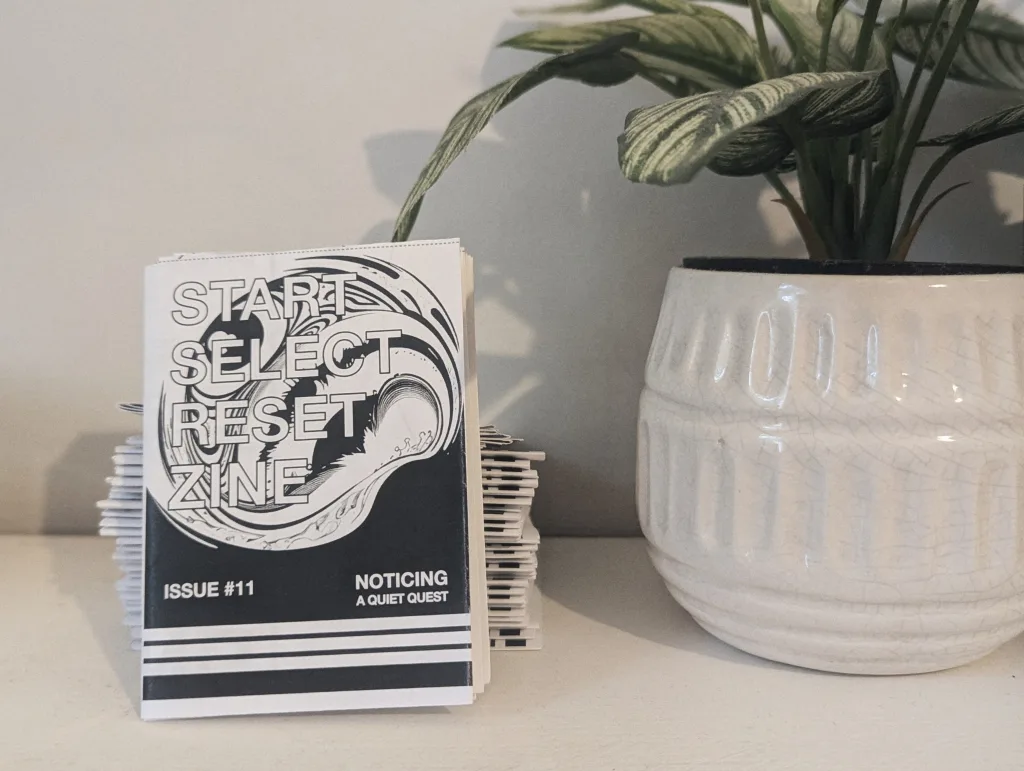 Stack of zines titled "Start Select Reset Zine" with issue number 011, featuring abstract black and white cover art, placed on a white surface.