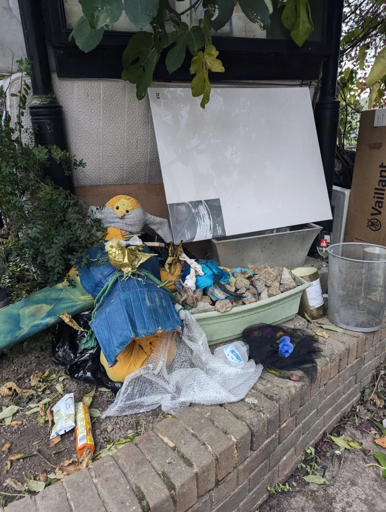 A big yellow plush bird wrapped in blue cardboard beside a blank white canvas, bubble wrap, and a planter of rocks on a brick ledge.