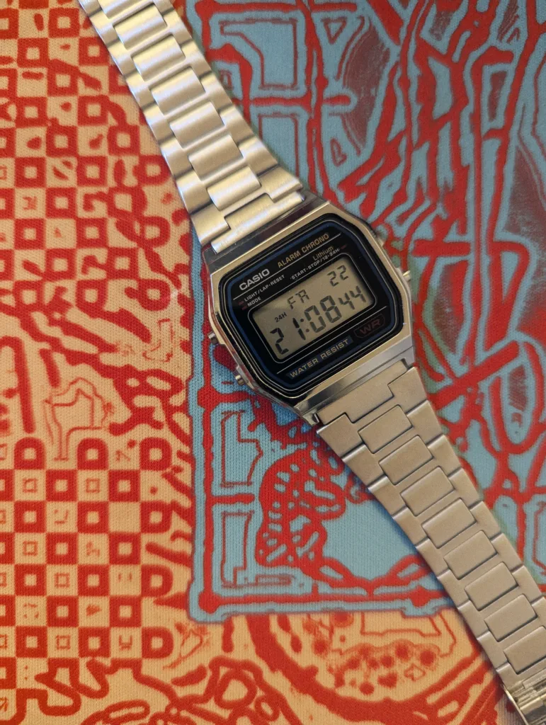 Silver Casio digital watch on a vibrant red and blue patterned fabric, displaying the time 21:08:44 on Friday the 22nd.