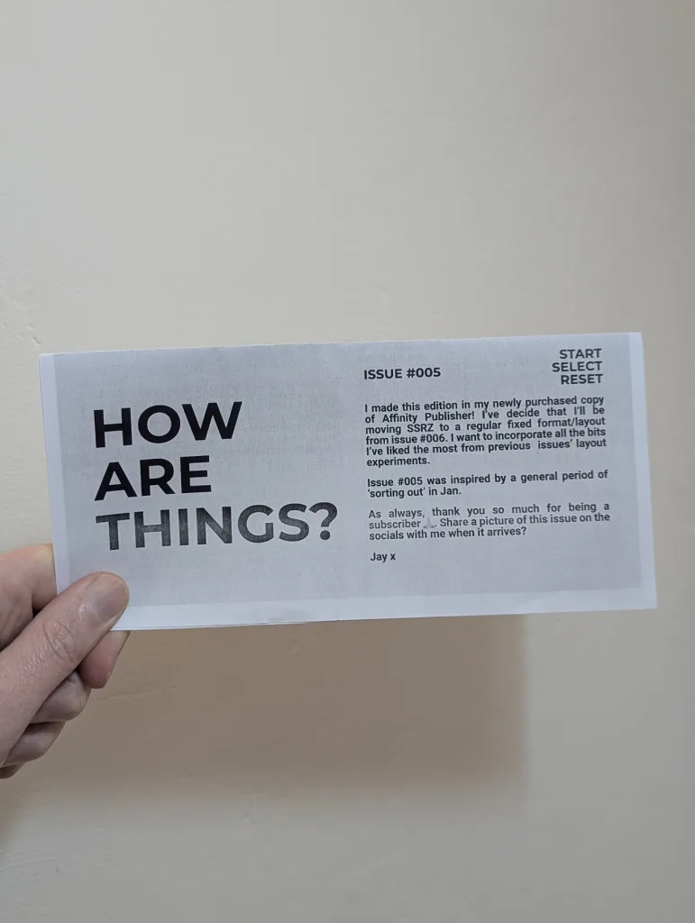 A hand holds a printed slip for SSRZ Issue #005 titled "HOW ARE THINGS?". Text notes the move to a fixed layout using Affinity Publisher.