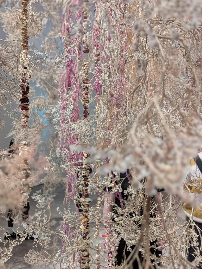 Vertical strands of dried pink and beige flowers and seed pods hanging in a dense, textured floral installation.