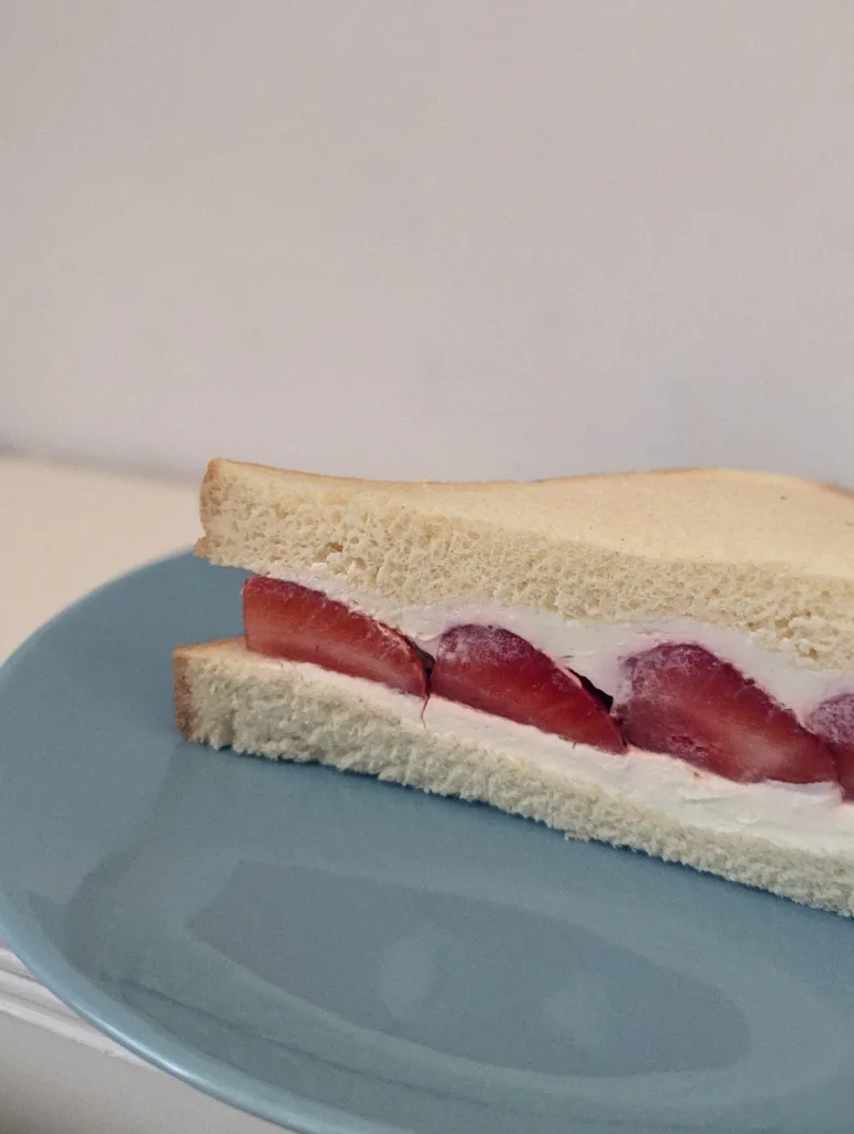 A Japanese fruit sandwich with large strawberry halves and whipped cream on white bread, served on a blue plate.