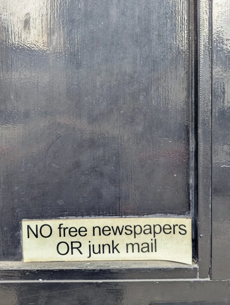 A cream sticker on a weathered black door reading "NO free newspapers OR junk mail".