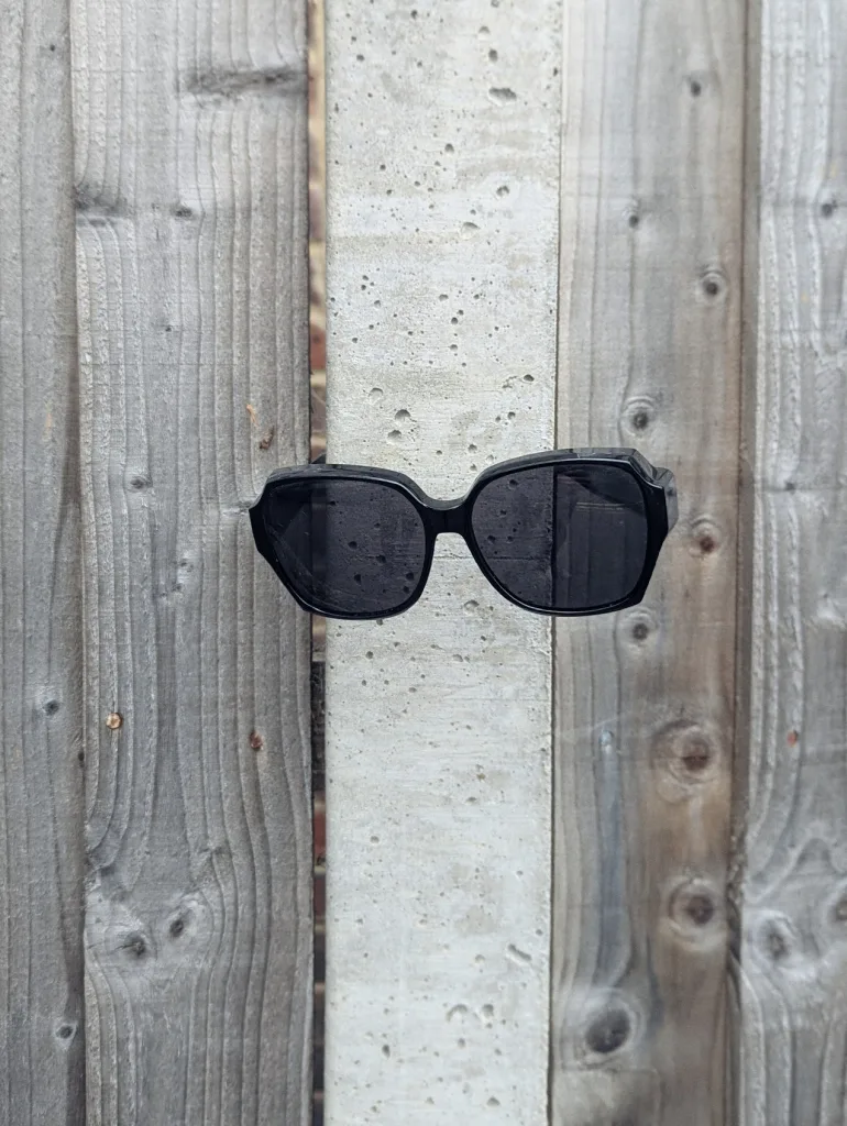 Thick-rimmed black sunglasses wedged into a concrete post in the middle of a weathered wooden fence.