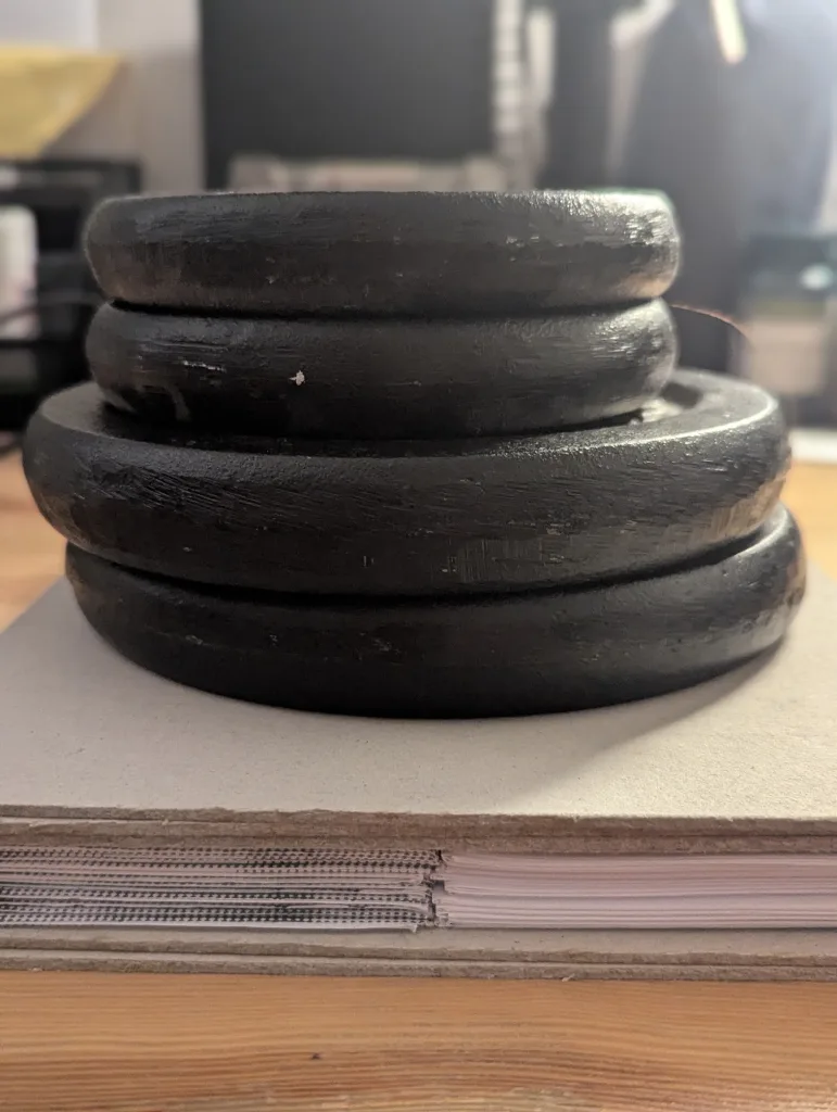 Four black iron weights of varying sizes stacked on a thick notebook on a wooden table.