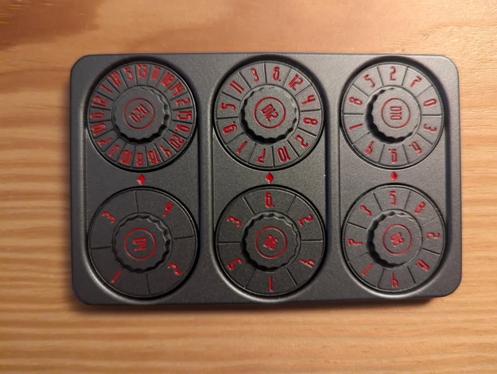 Matte black mechanical dice roller tool with six rotating dials labeled D20, D12, D10, D4, D6, and D8 in red on a wooden surface.