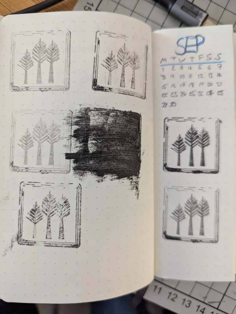 Stylized tree stamps and a hand-drawn September calendar in a dotted journal, with one stamp heavily smeared with black ink.