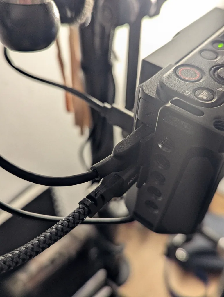 Close-up of several black cables and a braided HDMI cord plugged into the side ports of a Sony ZV-1 camera body housed in a metal cage.