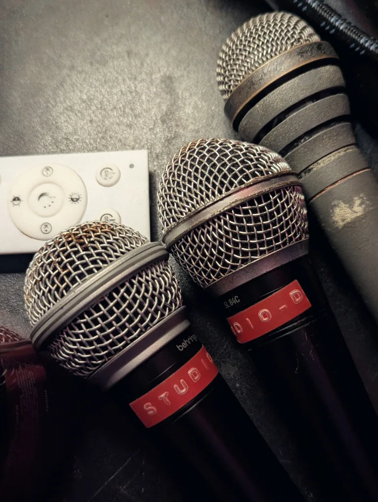Three microphones, two with red 'STUDIO' tape labels, on a dark surface next to a small white remote control.