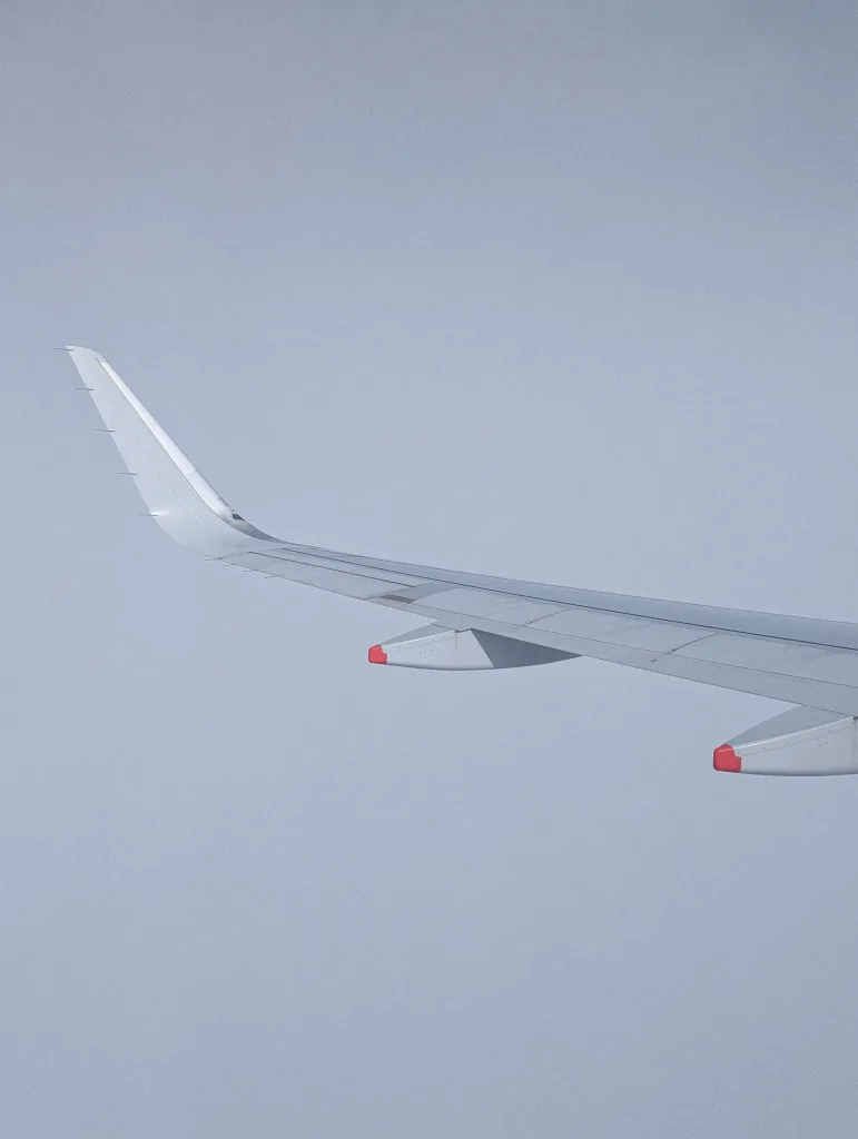 Airplane wing with an upward curved winglet and red-tipped fairings against a pale blue sky.