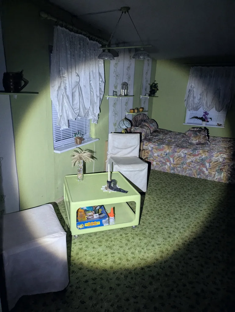 Flashlight beam illuminating a retro lime green bedroom with patterned carpet, floral bedding, and a square green coffee table.